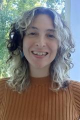 A person with medium long curly hair smiling brightly at the camera.