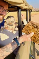 A person sitting in the back of a jeep in the desert holding a fragment of brown earth.