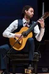 A performer playing the guitar on stage, seated.