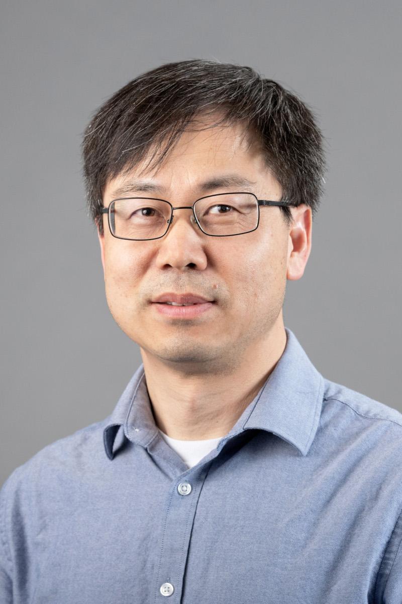 Fubing Su wearing glasses and a blue collared shirt, against a gray background.