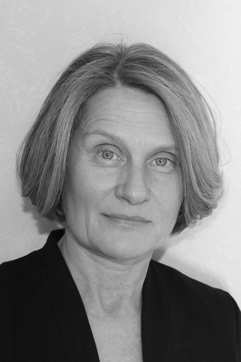 A monochrome headshot of Susan Hiner, a person with short light-colored hair and a dark jacket.
