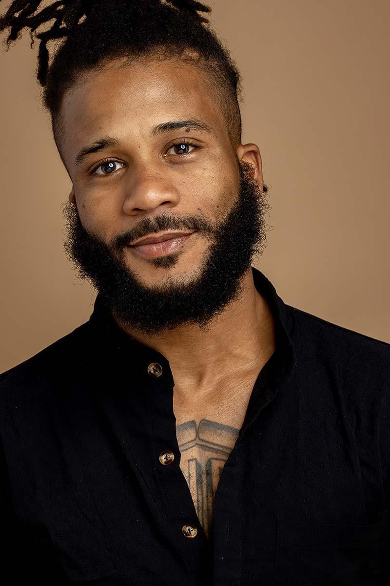 A photo of a person with dark, curly hair and beard, and a black shirt, looking at the camera