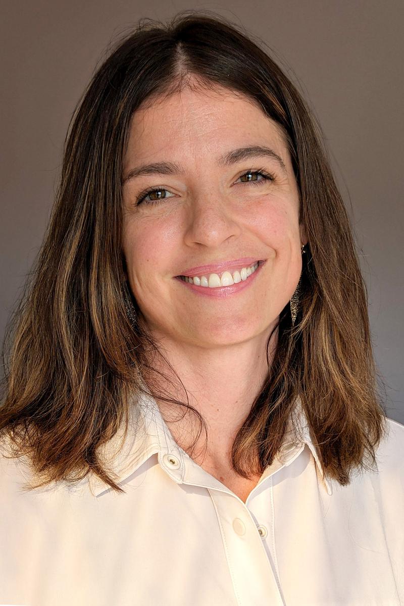 Person smiling with shoulder-length brown hair and a white button-up collared shirt.