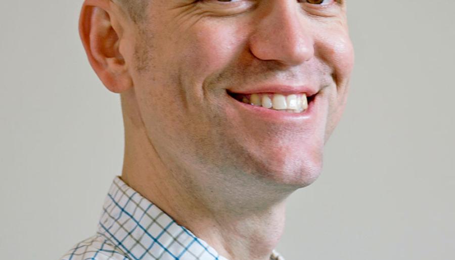 Justin C. Touchon wearing a white, square patterned shirt against a light background.