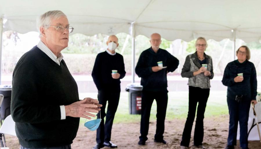 A group of retired faculty members stand under an outdoor tent