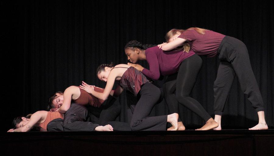Five women on a stage leaning on each other's backs in a line