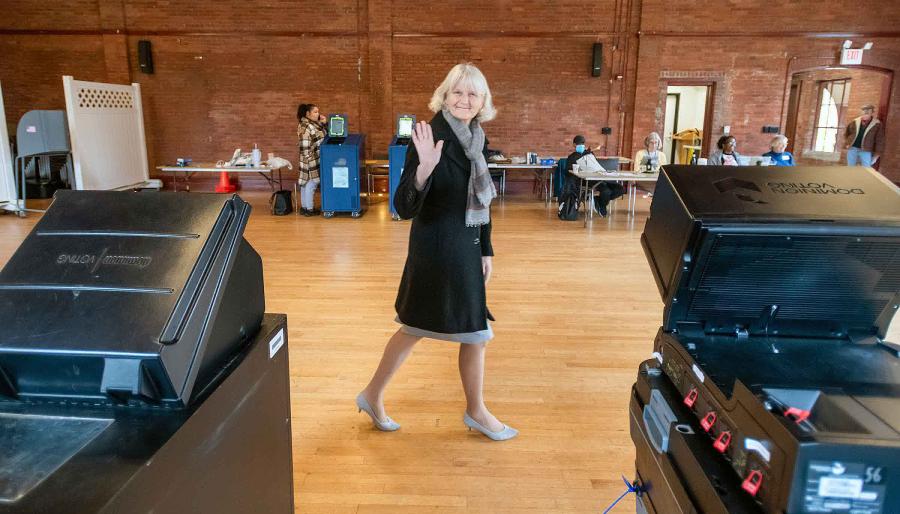 A person walking and waving to the camera at a polling site.