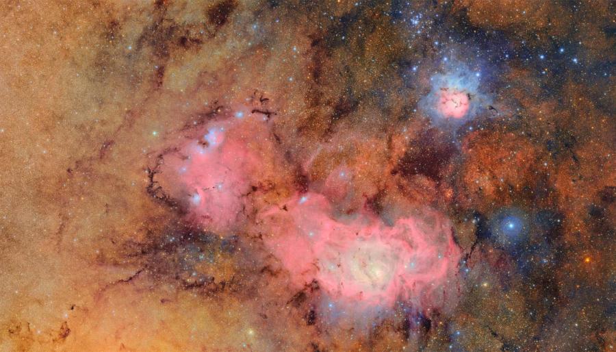 Orange and pink colors of the Trifid and Lagoon nebulas. Clouds of hydrogen emit a pink glow while hot stars shine blue.