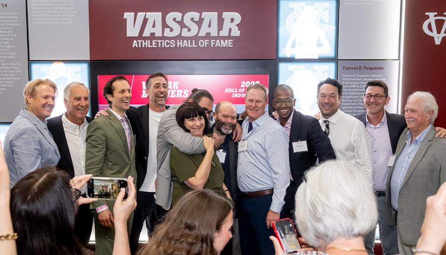 A celebratory group picture with a wall honoring the Hall of Fame inductees in the background.