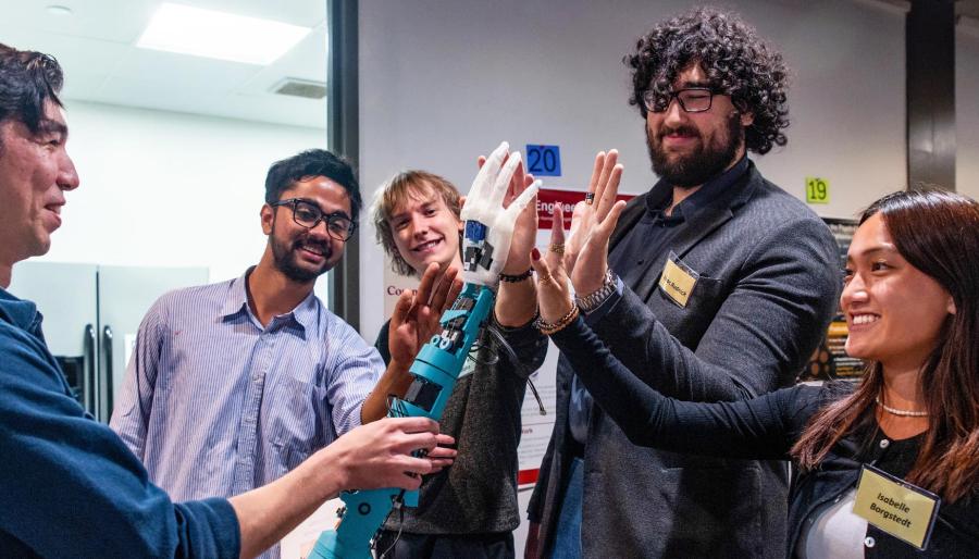 A group of onlookers checking out a robotic hand, held by a person, offerring a high five.