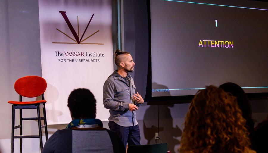 Person standing in front of a seated audience while addressing them.