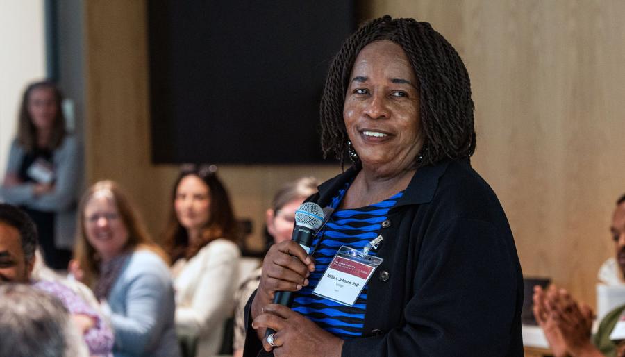 Person standing and speaking amid a seated smiling crowd.