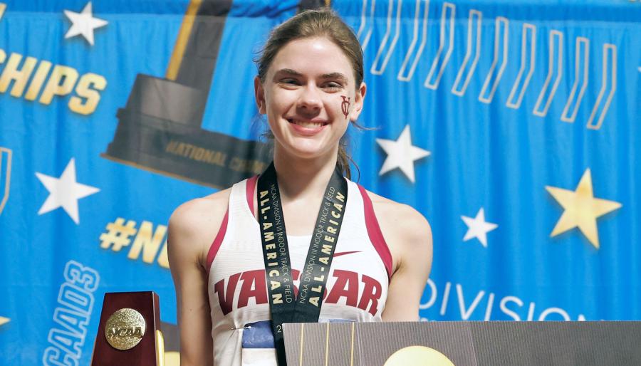 Smiling track athlete holding a trophy at an award ceremony.