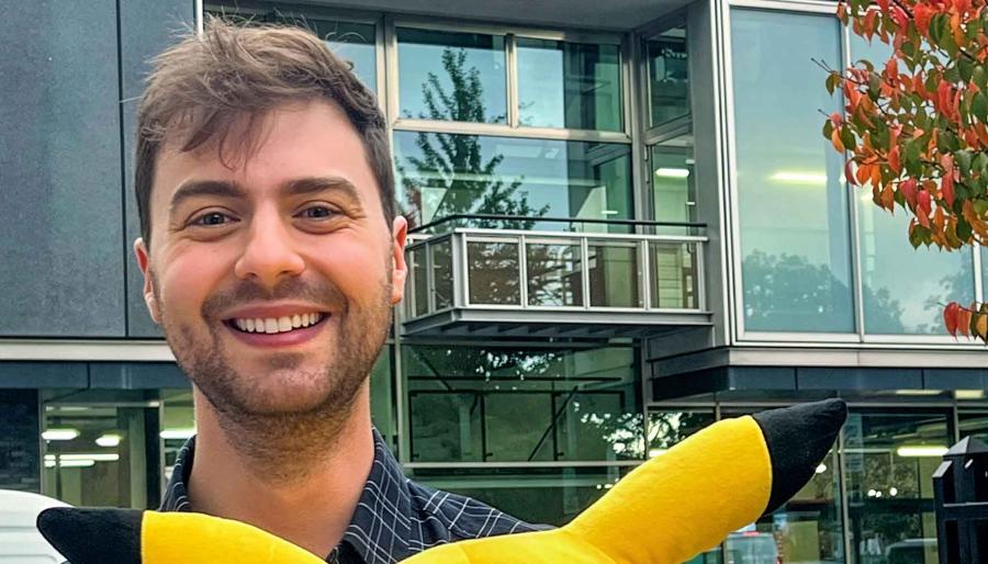 Person smiling in front of a building with Pokémon character ears at the bottom of the frame.