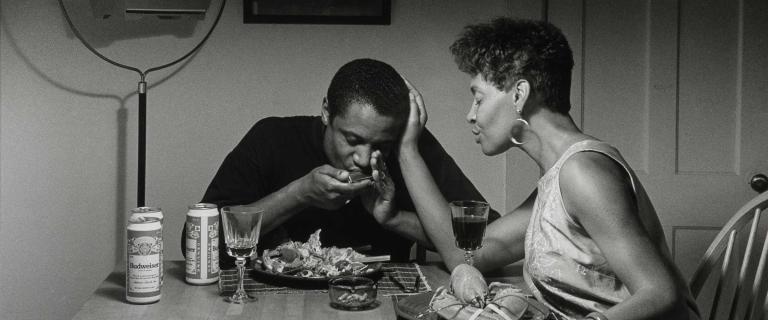 Black and white photo of two people having dinner in a room.