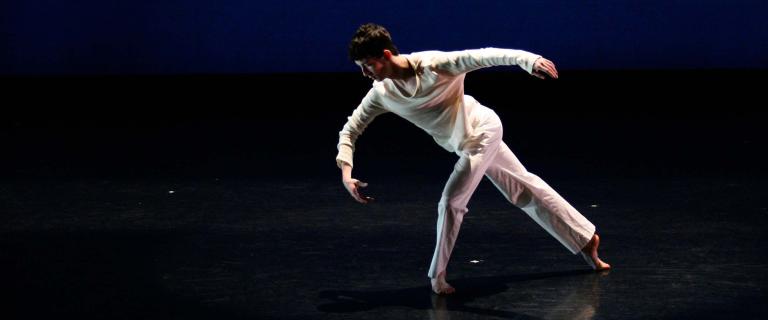 A person poses on a darkened stage.