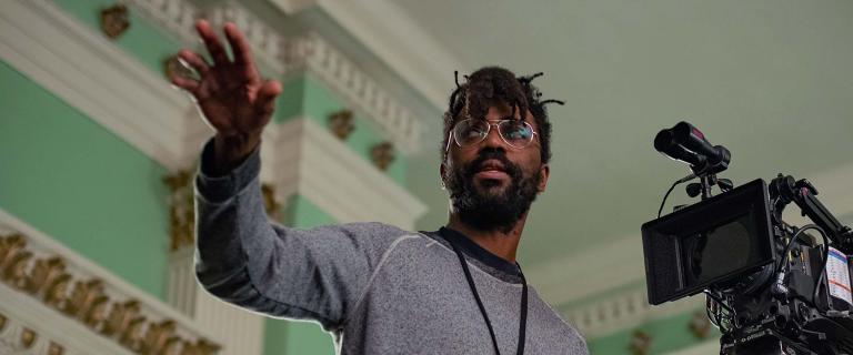 Director Shaka King ’01, standing behind a camera, giving direction to people off screen