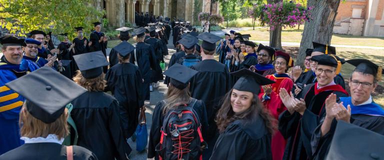 Students in black caps and gowns in procession with Professors in caps and gowns on the sides at Vassar College Convocation.