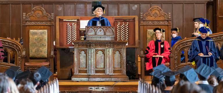 Elizabeth H. Bradley, PhD, wearing a black cap and blue gown speaking at the podium at Vassar College Convocation.