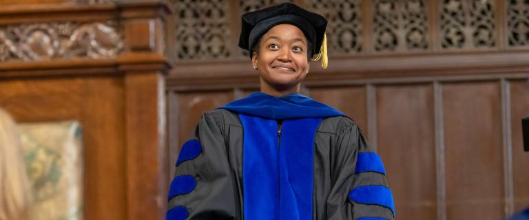 Kelli Duncan wearing a black cap and gray gown with blue stole at Vassar College Convocation.