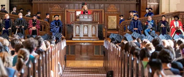 Nancy Bisaha wearing red gown speaking at the podium at Vassar College Convocation.