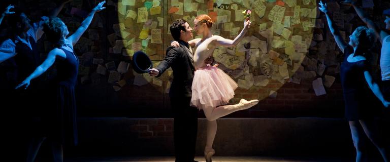 Dancer and ballerina on stage in a spotlight surrounded by other dancers