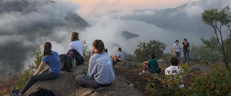 People sitting on mountain looking down at fogged river valley