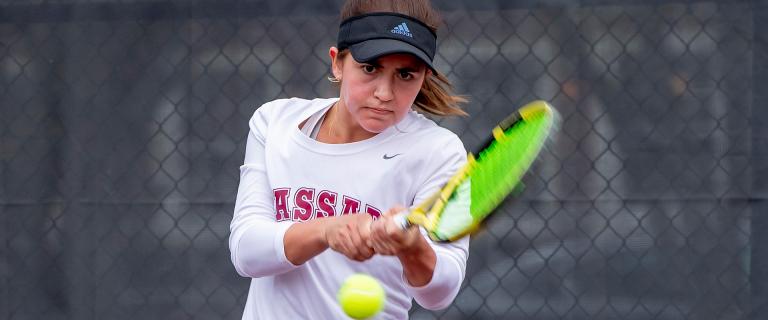 Pictured: Macey Dowd ’25 - Woman hitting a two-handed backhand on a tennis court.