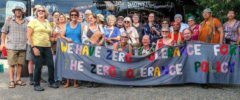 Large group shot of people in front of a bus holding a banner that reads: We have zero tolerance for the zero tolerance policy