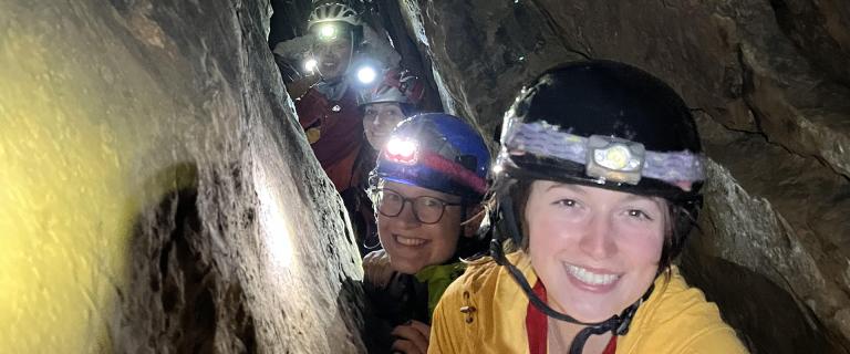 People climbing in a dark cave with hardhats with flashlights on them.