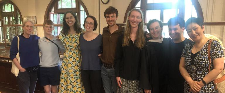 A group of students and a professor standing in front of arched glass windows.