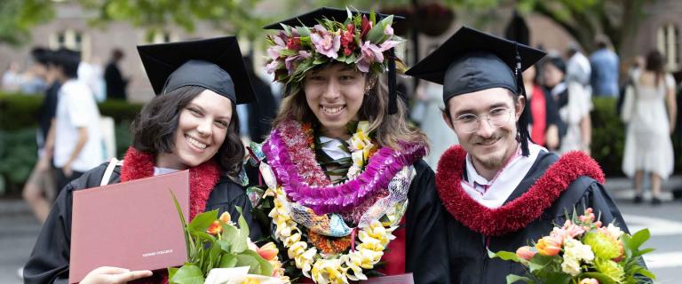 Graduates smiling arm in arm holding their diplomas