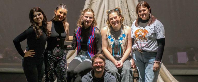 group of drama personnel smiling and posing for a photo on a stage 