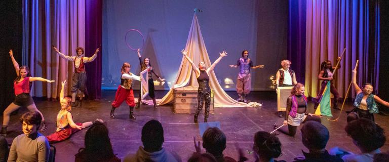 stage with actors with arms spread wide in front of an audience