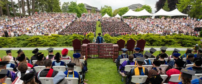 panoramic shot of graduation ceremony from behind showing seated attendees and the stage with all the people