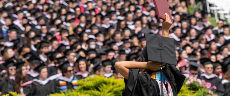 Graduate with back to camera holding up their diploma in front of audience