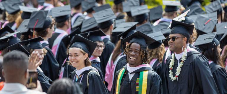 Smiling graduates in the crowd wearing caps and gowns and sunglasses