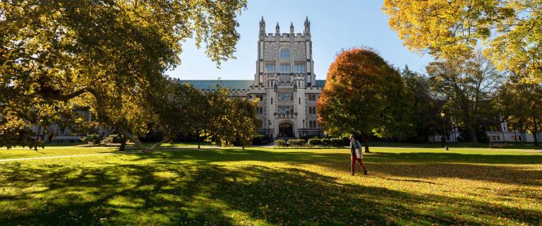 Pictured: Vassar Library. An old light colored brick building with a castle style towner in the center. There are green trees and grass in the foreground.