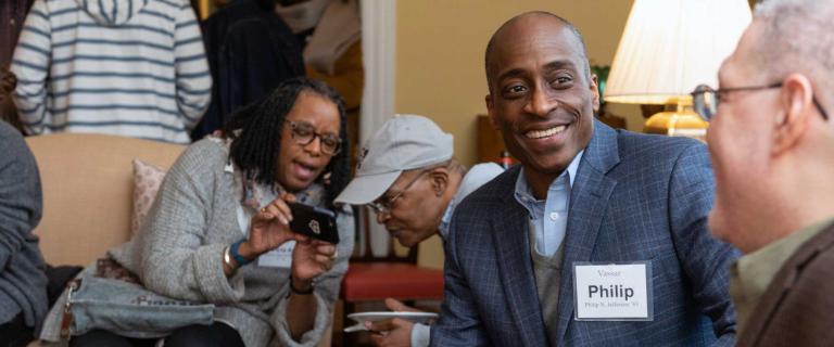 Philip Jefferson seated in the foreground talking to another person while two people in the background look at a phone screen.