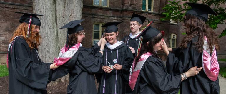 Group of people in graduation ceremony attire adjusting each other's tassels, robes and mortar boards.