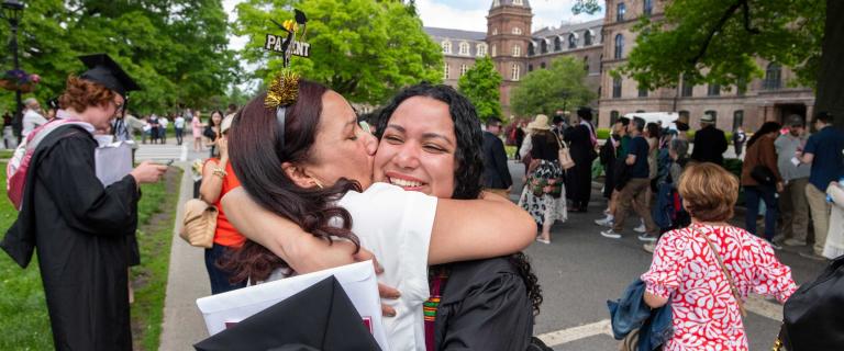 A person with a hair ornament that says "Parent" hugging someone in graduation ceremony attire.