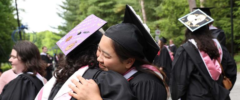 Two people in graduation ceremony attire hugging.