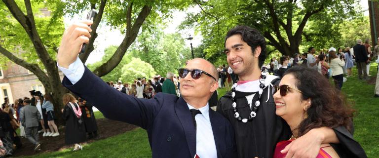 Three people smiling and posing for a selfie at a graduation ceremony.
