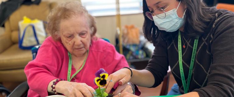 Two people at a table working together to plant a seedling.