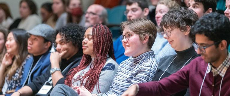 A line of people seated in an audience smiling and listening.
