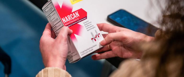 A detail of a person holding a box labeled narcan.
