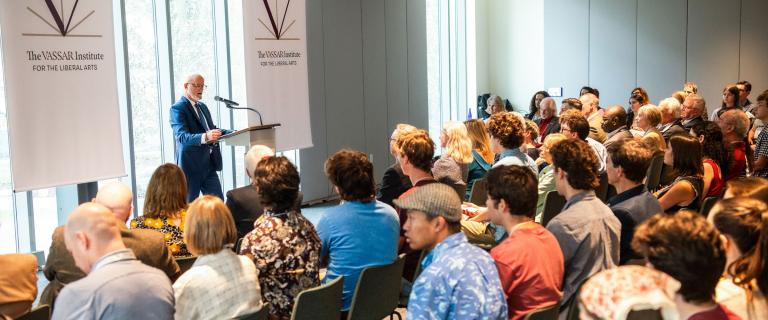 Person standing at a podium speaking into a microphone in front of an audience.