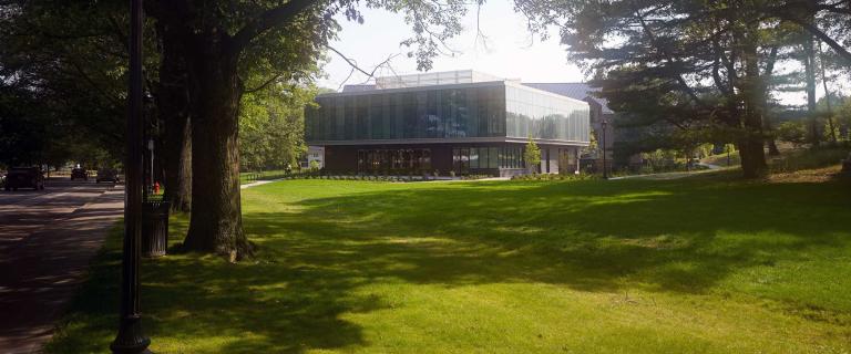 Exterior photo of a building surrounded by large trees and a grass lawn.