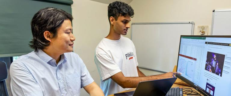 A student and mentor discuss data analysis shown on a large monitor.