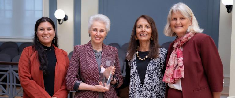 Four standing people smiling, one holding an award.